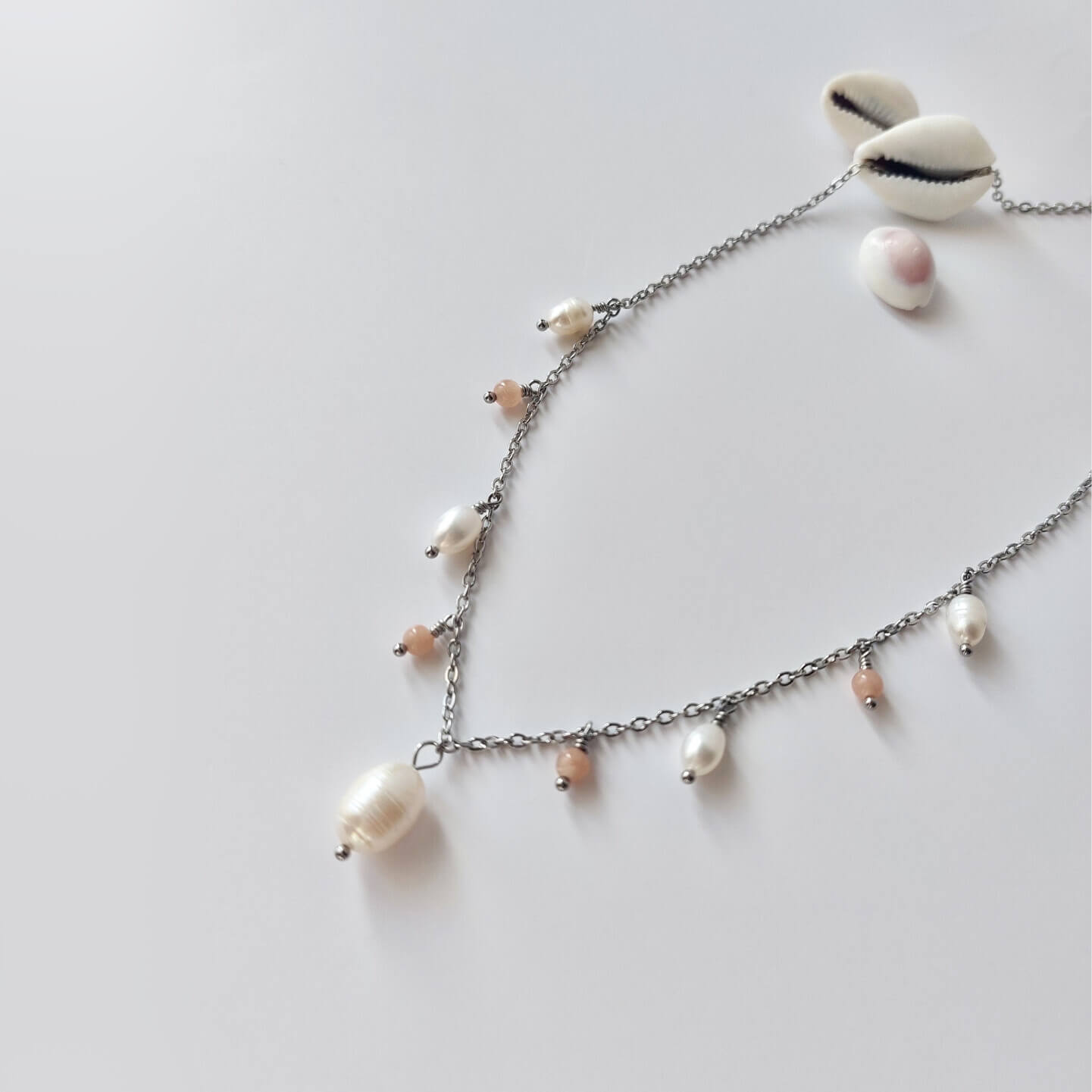 Collier Meandrina en acier inoxydable argenté, perles d'eau douce et perles de pierre de soleil roses posé sur fond blanc