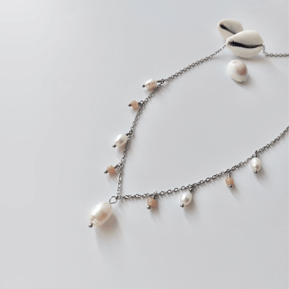 Collier Meandrina en acier inoxydable argenté, perles d'eau douce et perles de pierre de soleil roses posé sur fond blanc