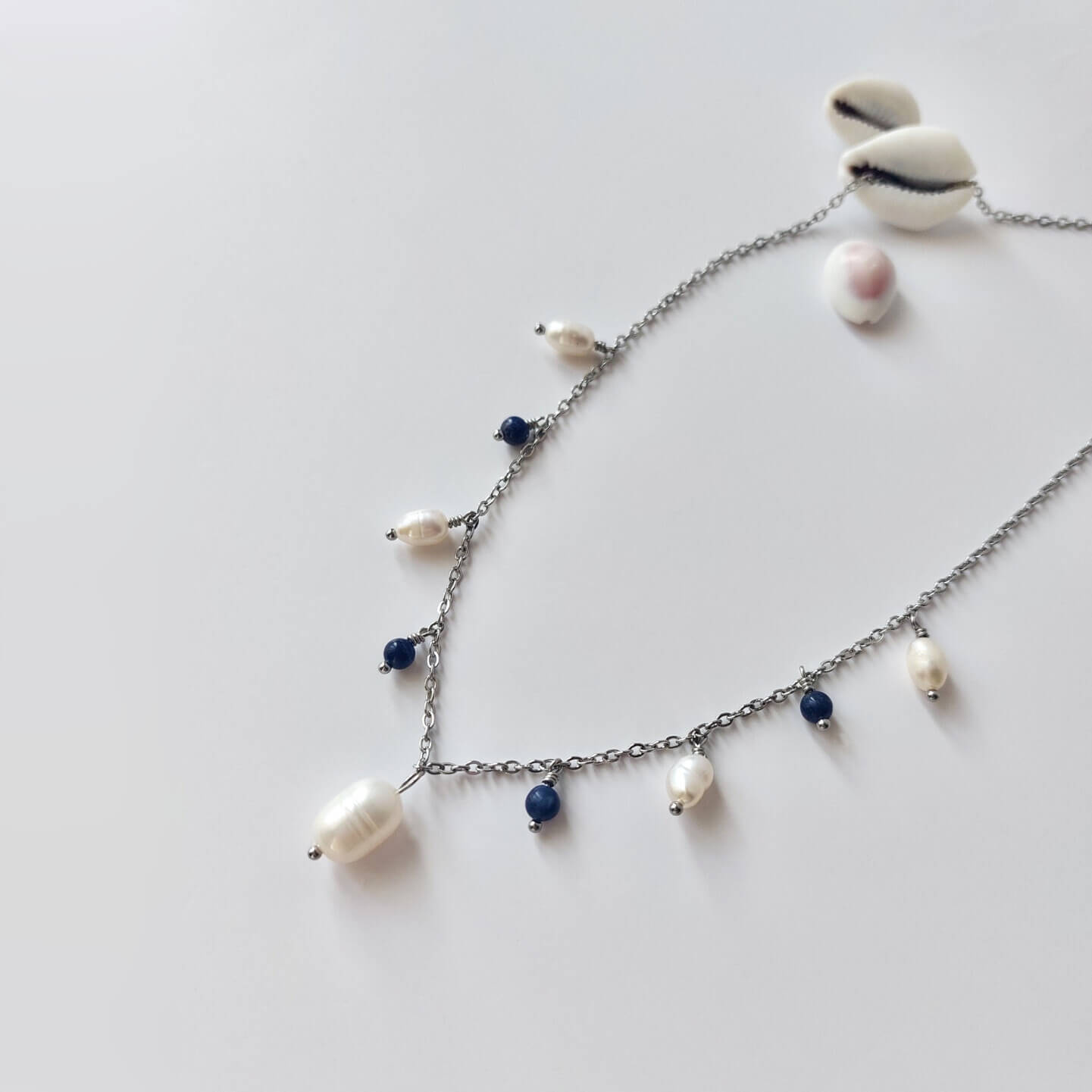 Collier Meandrina en acier inoxydable argenté, perles d'eau douce et perles de sodalite bleue posé sur fond blanc