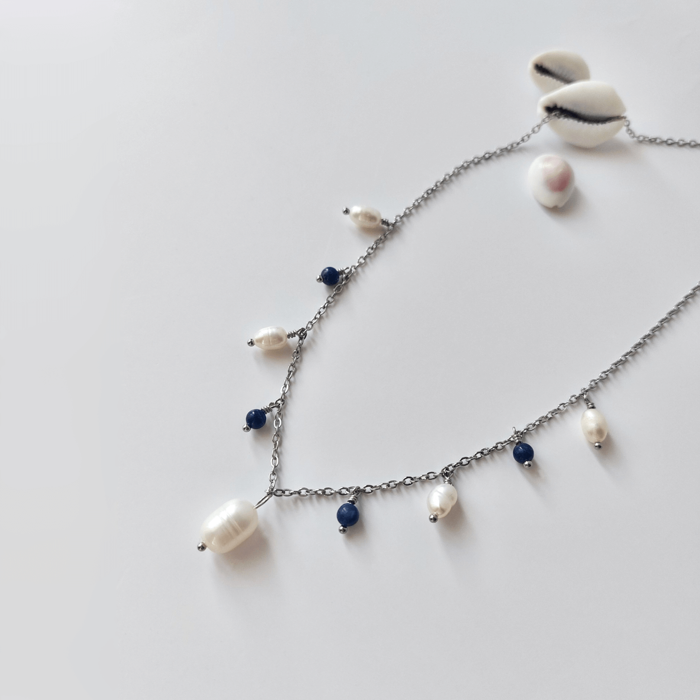 Collier Meandrina en acier inoxydable argenté, perles d'eau douce et perles de sodalite bleue posé sur fond blanc
