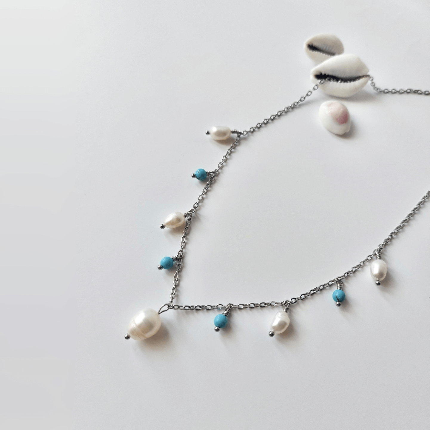 Collier Meandrina en acier inoxydable argenté, perles d'eau douce et perles de turquoise bleue posé sur fond blanc