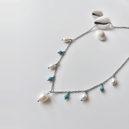 Collier Meandrina en acier inoxydable argenté, perles d'eau douce et perles de turquoise bleue posé sur fond blanc