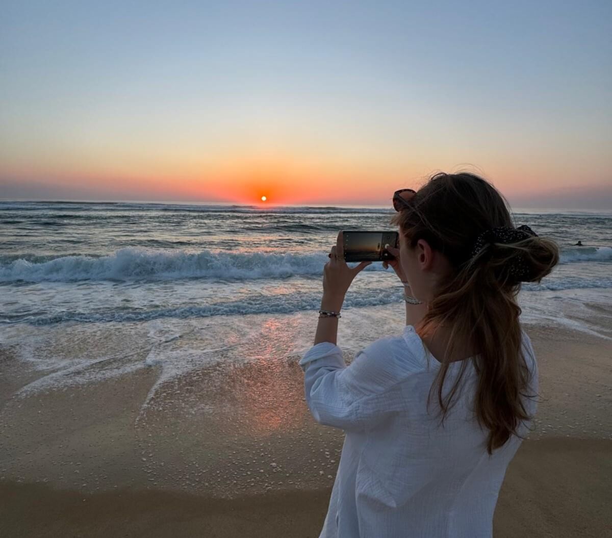 Une femme photographiant le coucher de soleil sur la plage