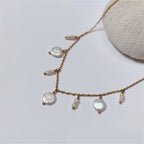 Collier en acier inoxydable doré avec perles d’eau douce plates et petits trios de perles blanches, posé sur un corail blanc, sur fond blanc.