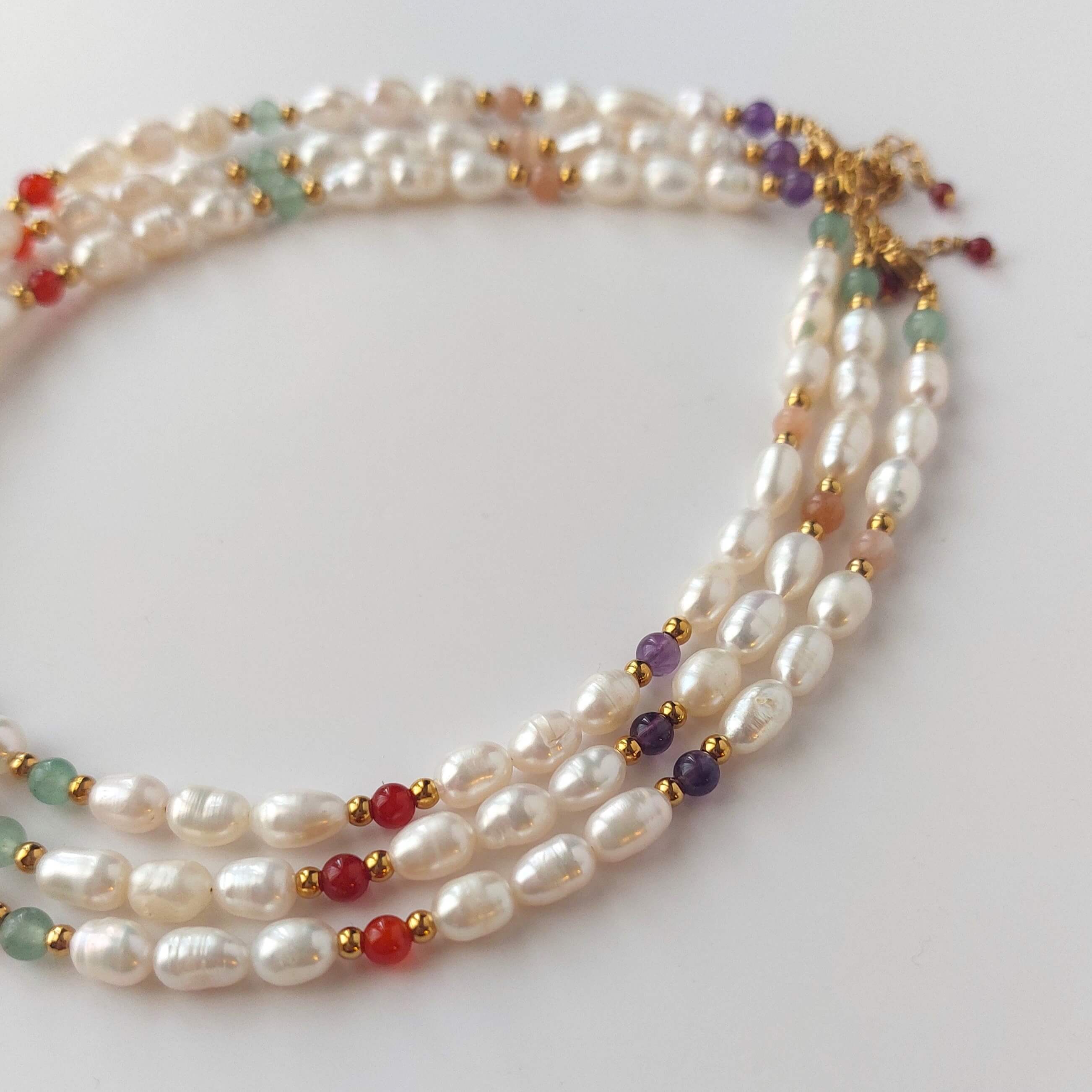 Collier ras de cou en perles d'eau douce et pierres naturelles colorées posé sur fond blanc